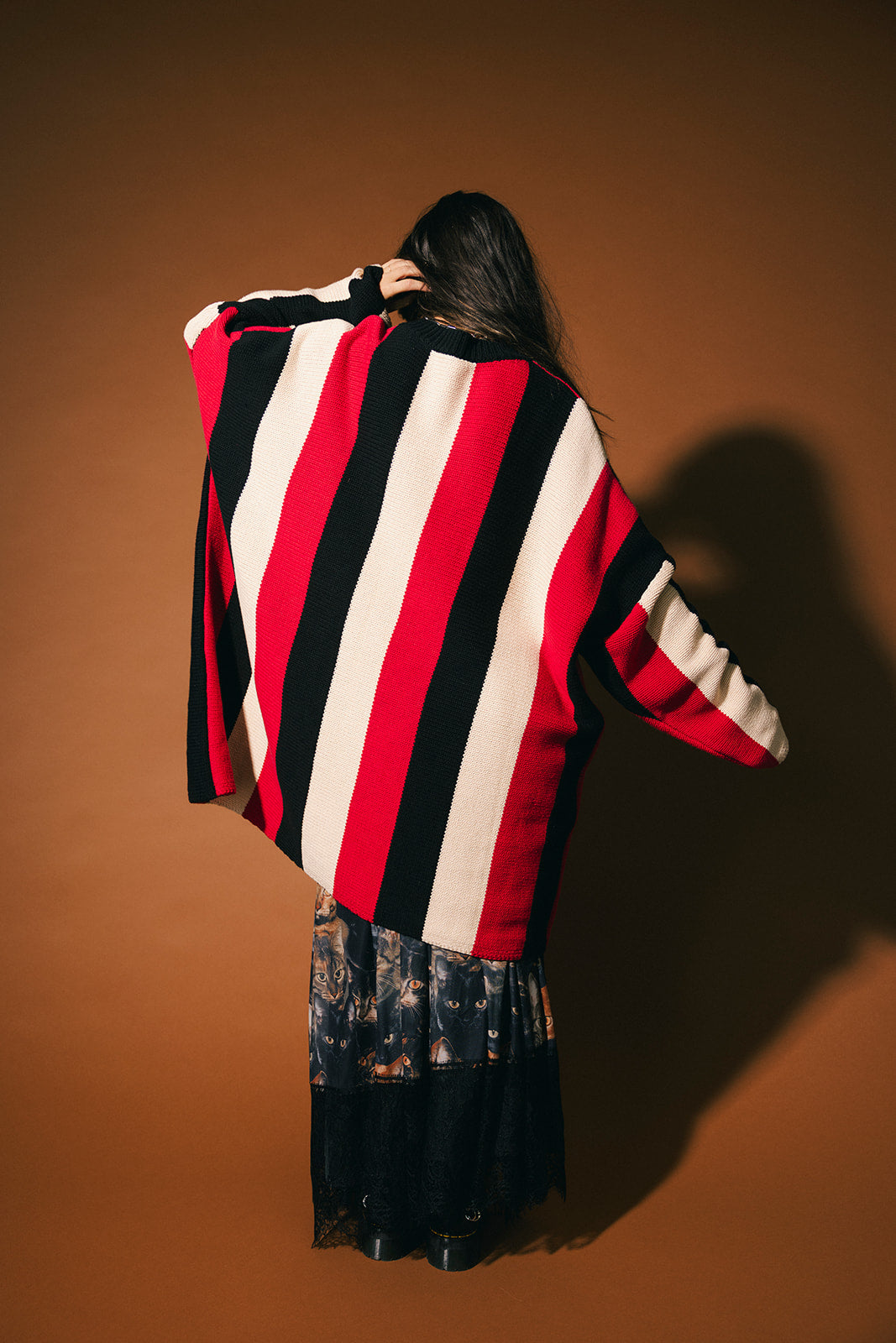 Person wearing a red, black, and white oversized striped sweater against a brown background