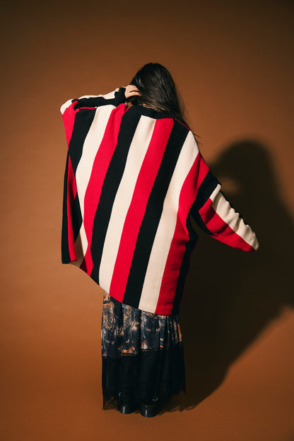 Person wearing a red, black, and white oversized striped sweater against a brown background