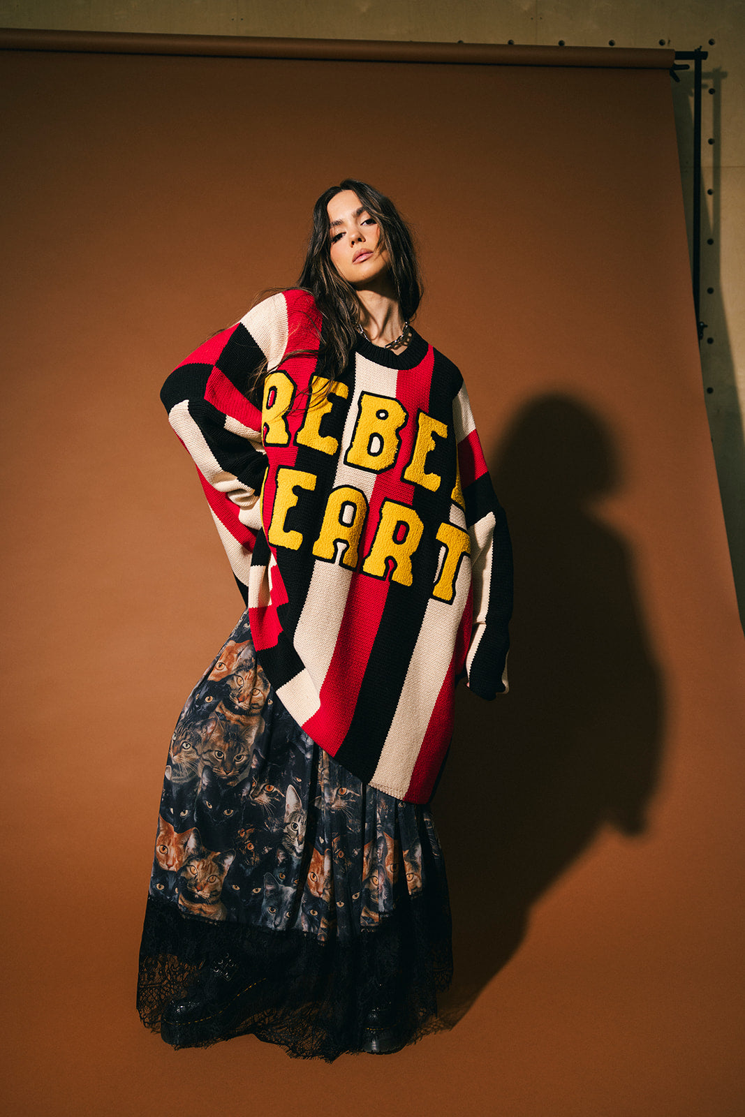 Woman wearing an oversized striped sweater with 'Rebel Heart' text in patches against a brown background