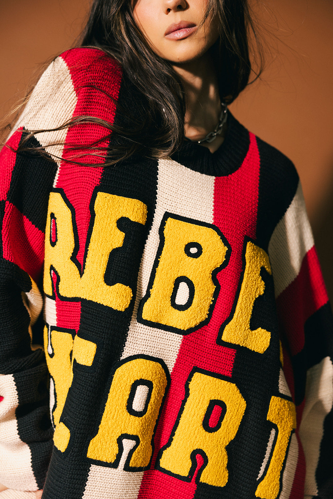 Person wearing an oversized striped sweater with 'Rebel Heart' in patches
