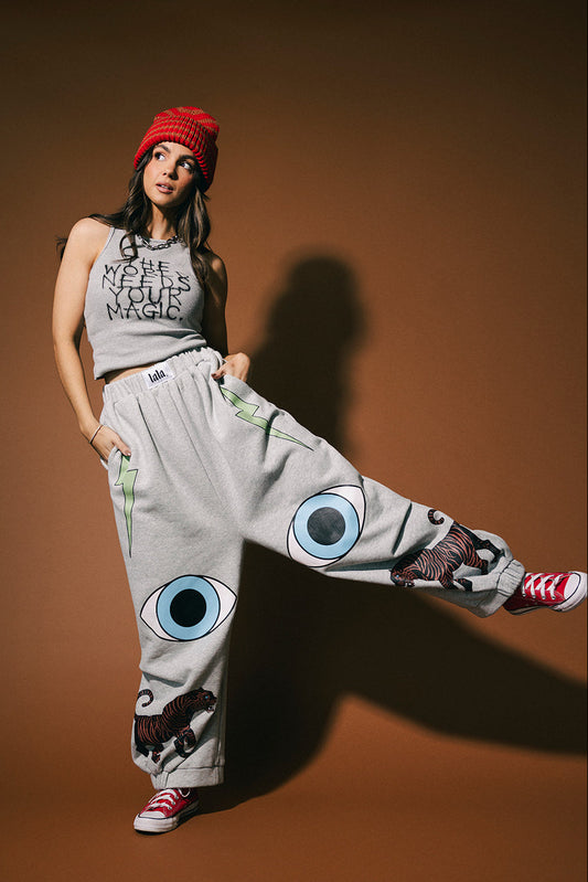 Person wearing a tank top and heather grey drop crotch barrel leg pants with graphic designs on a brown background