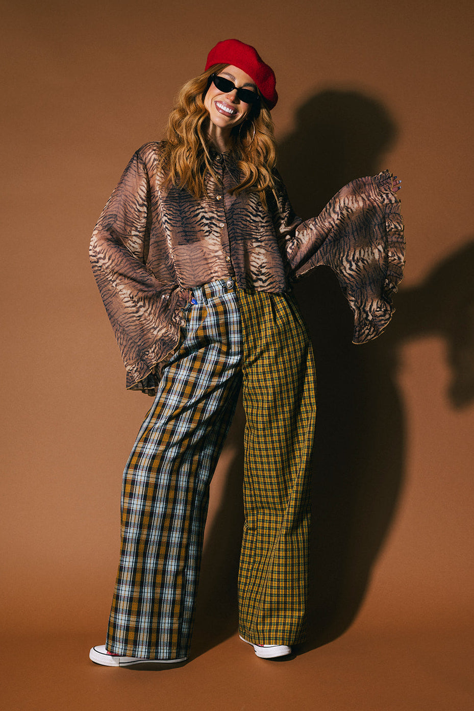 Person wearing a sheer tiger print button up top with flowy sleeves on a brown background