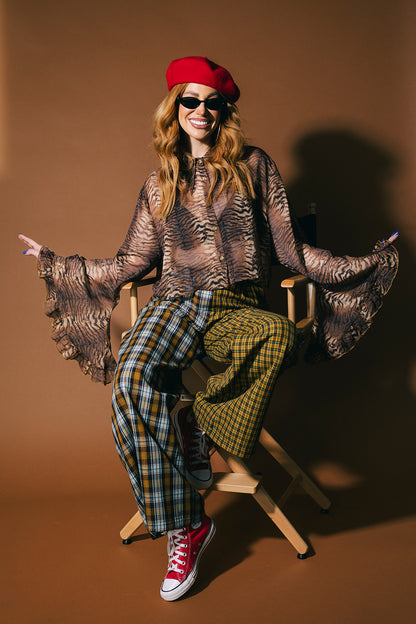 Person wearing a sheer tiger print button up top with flowy sleeves on a brown background