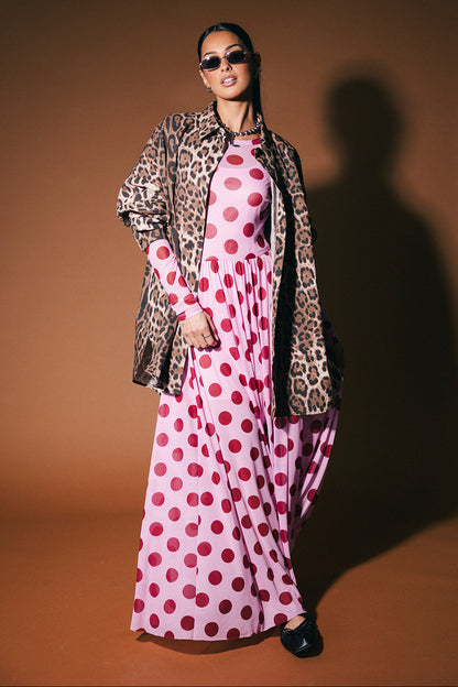 Woman wearing a leopard print button up over a pink polka dot dress on a brown background