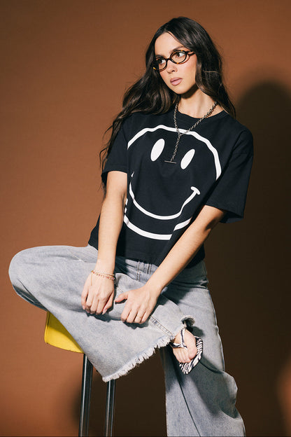 Person wearing a black t-shirt with a smiley face design against a brown background