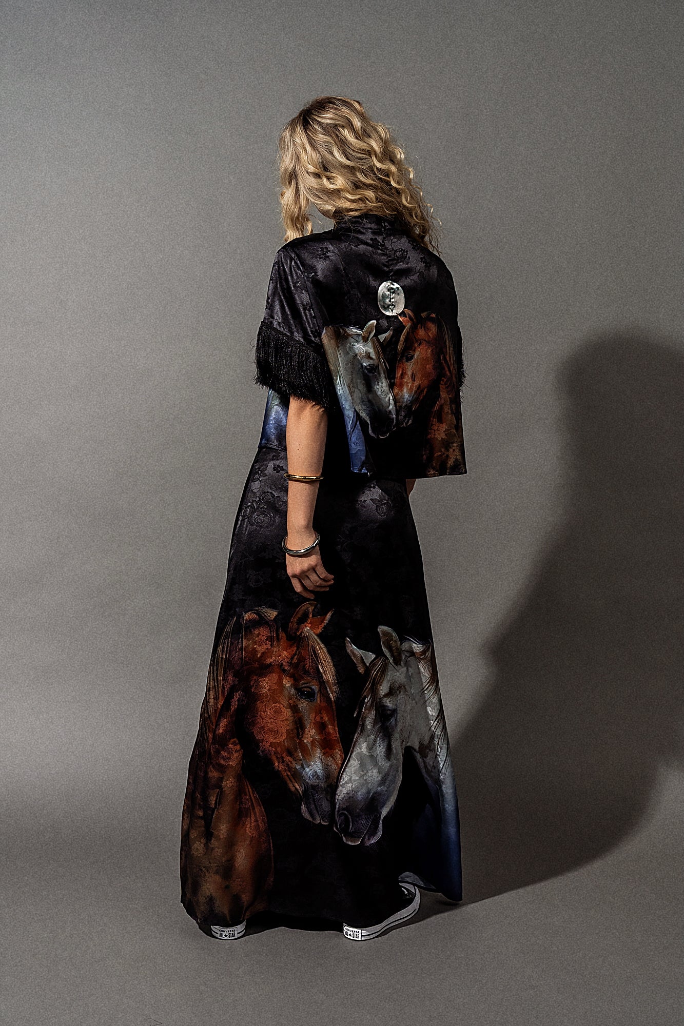 Person wearing a long, dark dress with horse designs on a gray background
