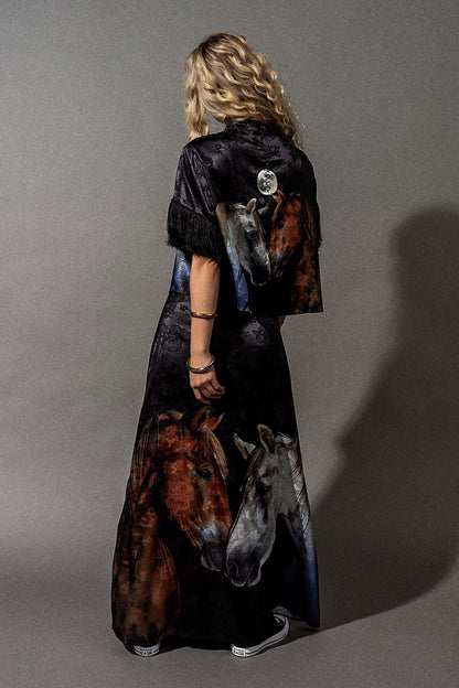 Person wearing a long, dark dress with horse designs on a gray background 