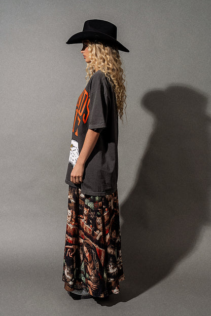 Person wearing a black hat, gray t-shirt with orange text, and patterned pants against a gray background