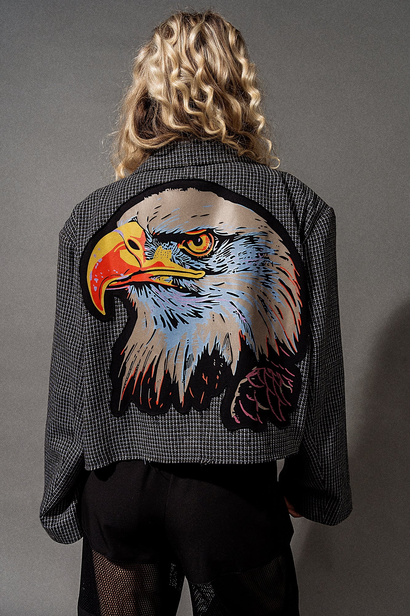 Person wearing a jacket with an eagle design on the back against a gray background