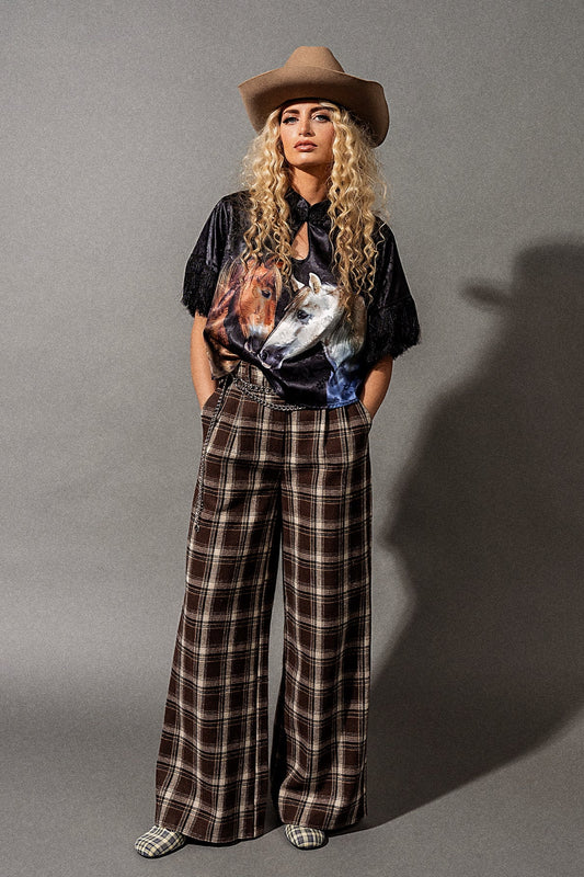 Person wearing a cowboy hat, graphic t-shirt, and plaid pants on a gray background