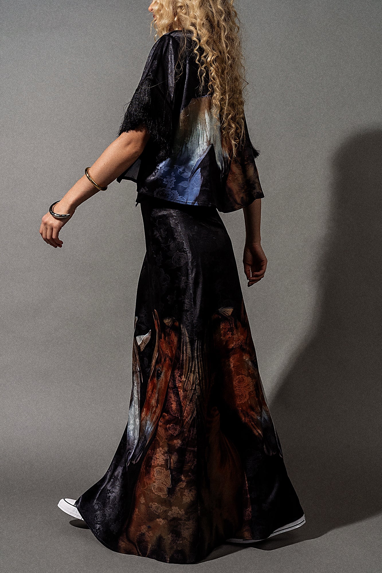 Person wearing a long, dark-colored dress with abstract patterns on a gray background