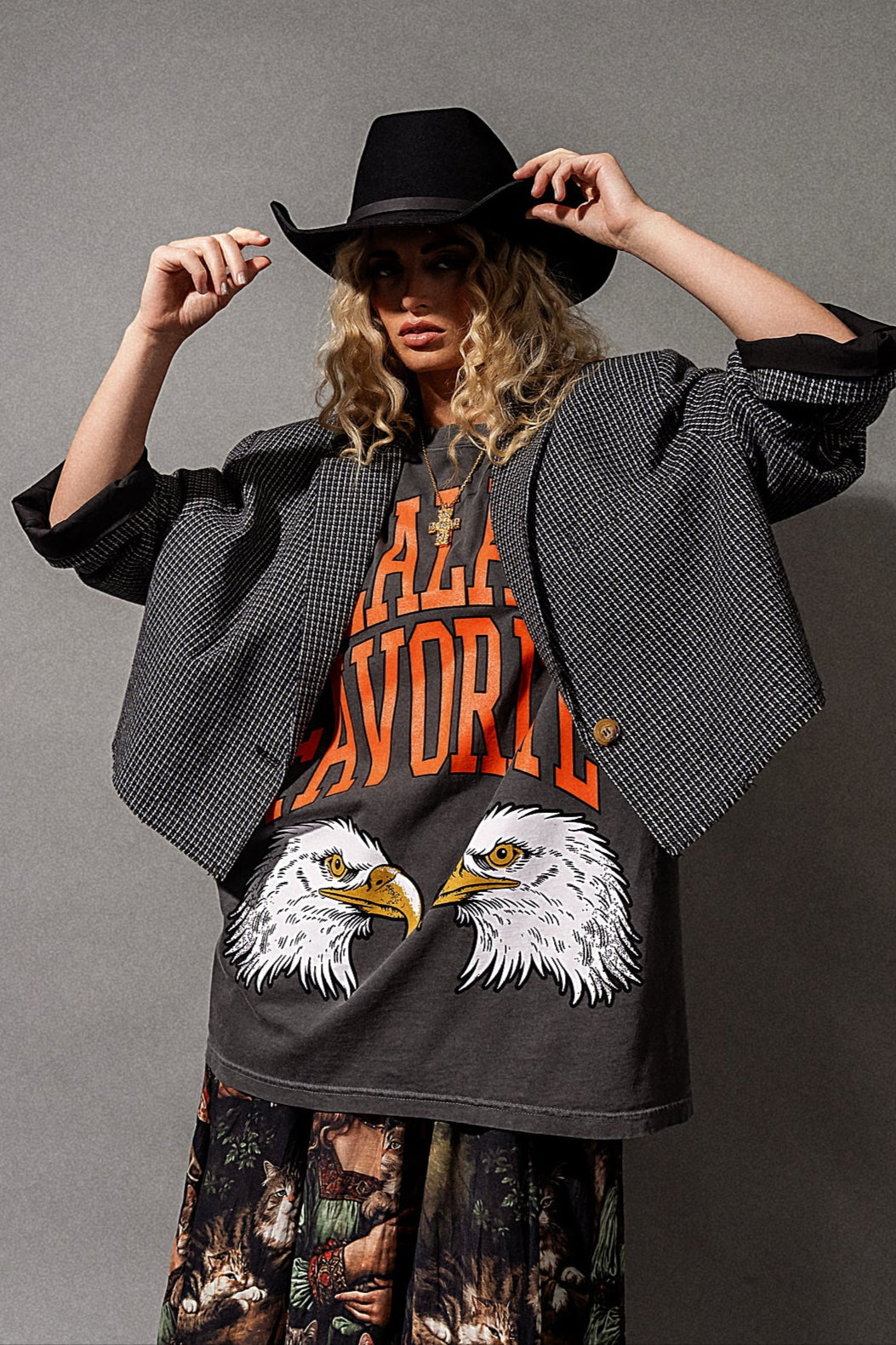 Person wearing a black blazer, graphic t-shirt, and black hat on a gray background
