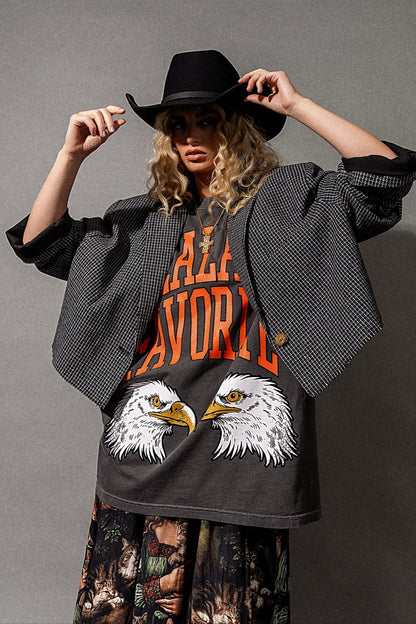 Person wearing a black blazer, graphic t-shirt, and black hat on a gray background