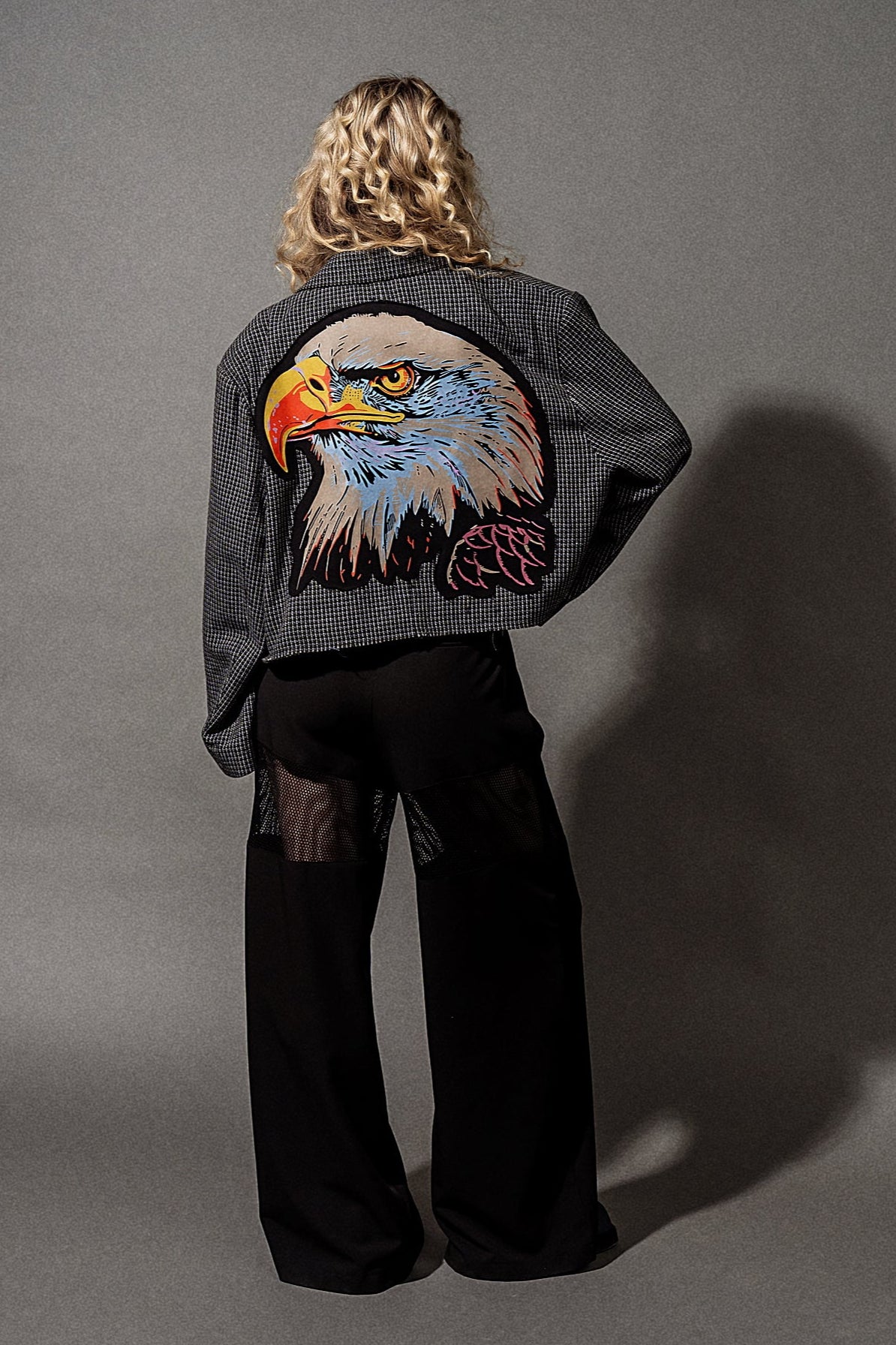 Person wearing a jacket with an eagle design on the back against a gray background