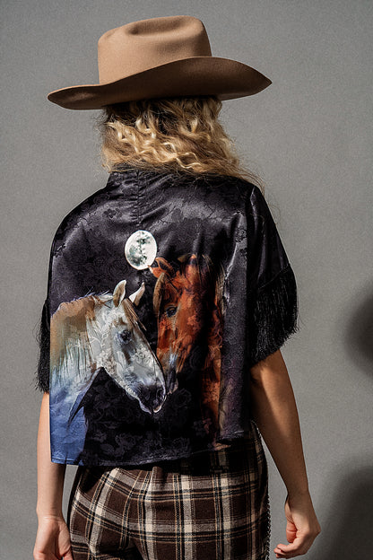 Person wearing a black shirt with a horse design, plaid pants, and a cowboy hat on a gray background