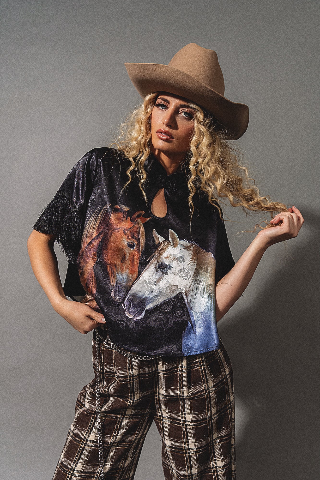 Woman wearing a black t-shirt with horse designs and a brown cowboy hat on a gray background