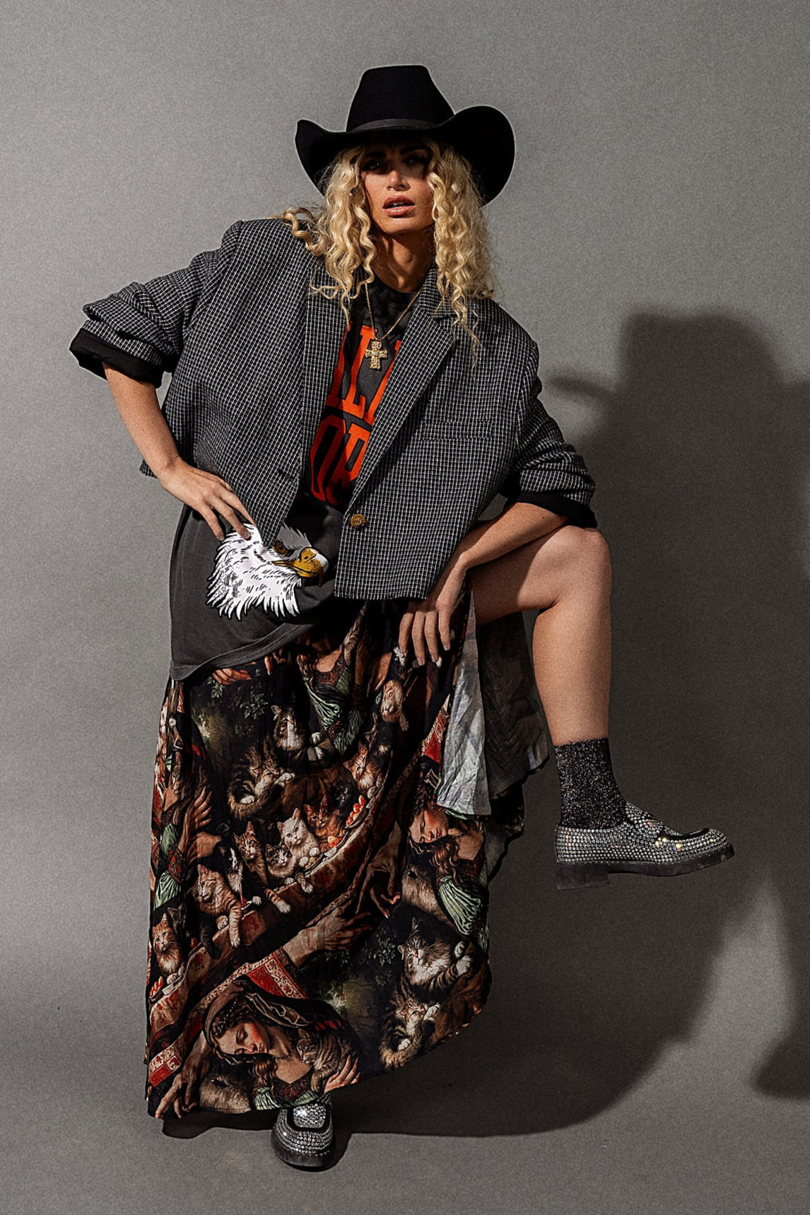 Person wearing a gray blazer, floral skirt, and cowboy hat against a gray background