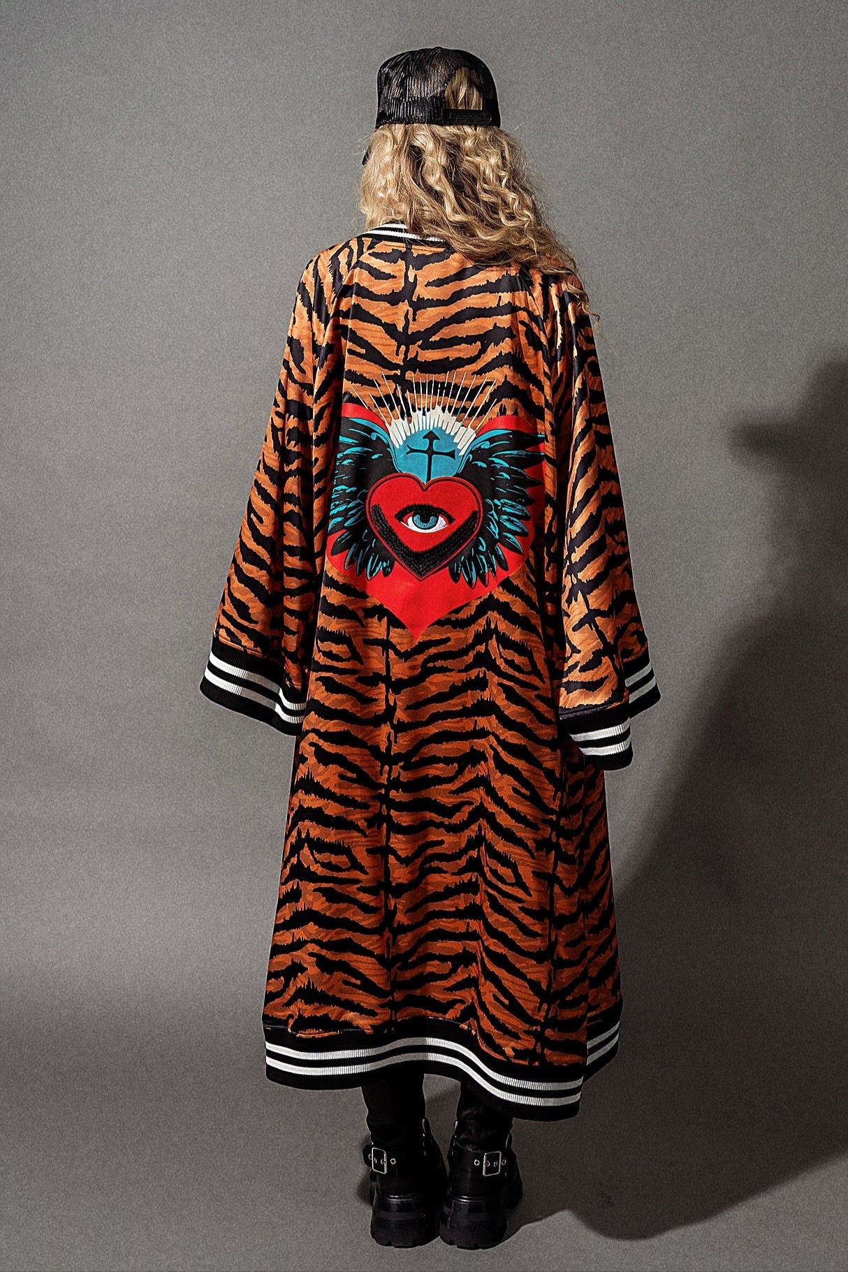 Person wearing a tiger-striped coat with a colorful heart design on a gray background