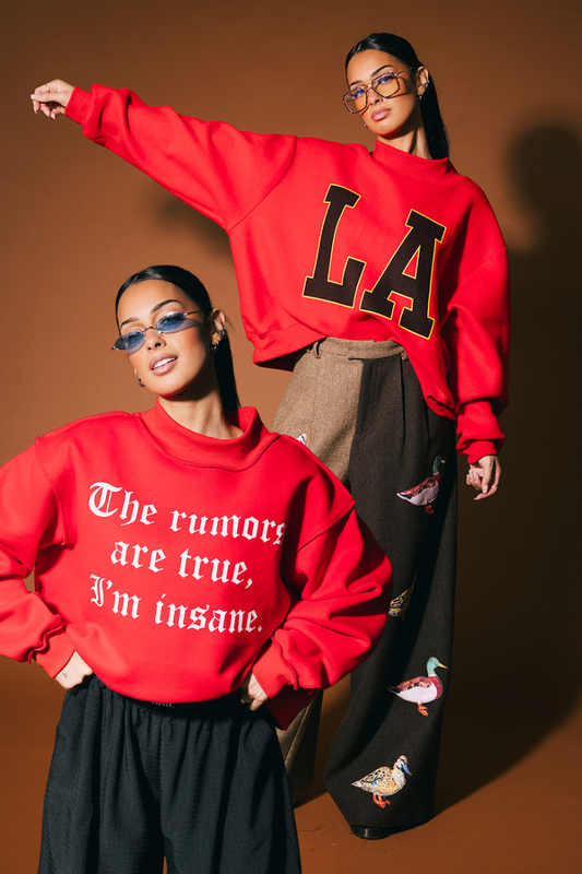 Photo showing woman wearing a reversible red sweatshirt with text, standing against a brown background.