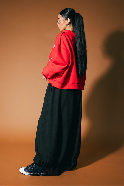 Person wearing a red sweatshirt and black pants against a brown background