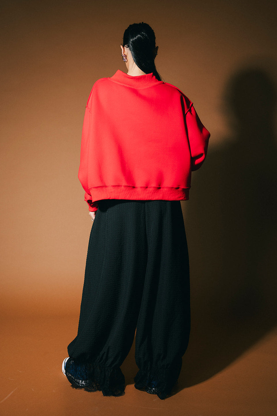 Person wearing a red sweatshirt and black pants standing against a brown background