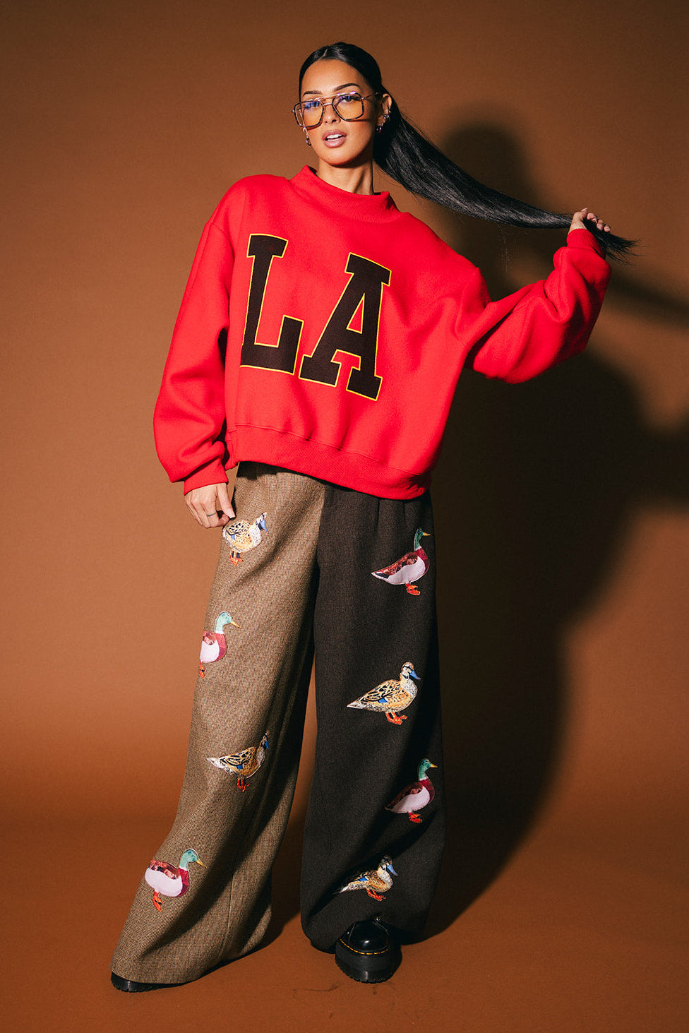 Person wearing a red 'LA' sweatshirt and patterned pants on a brown background