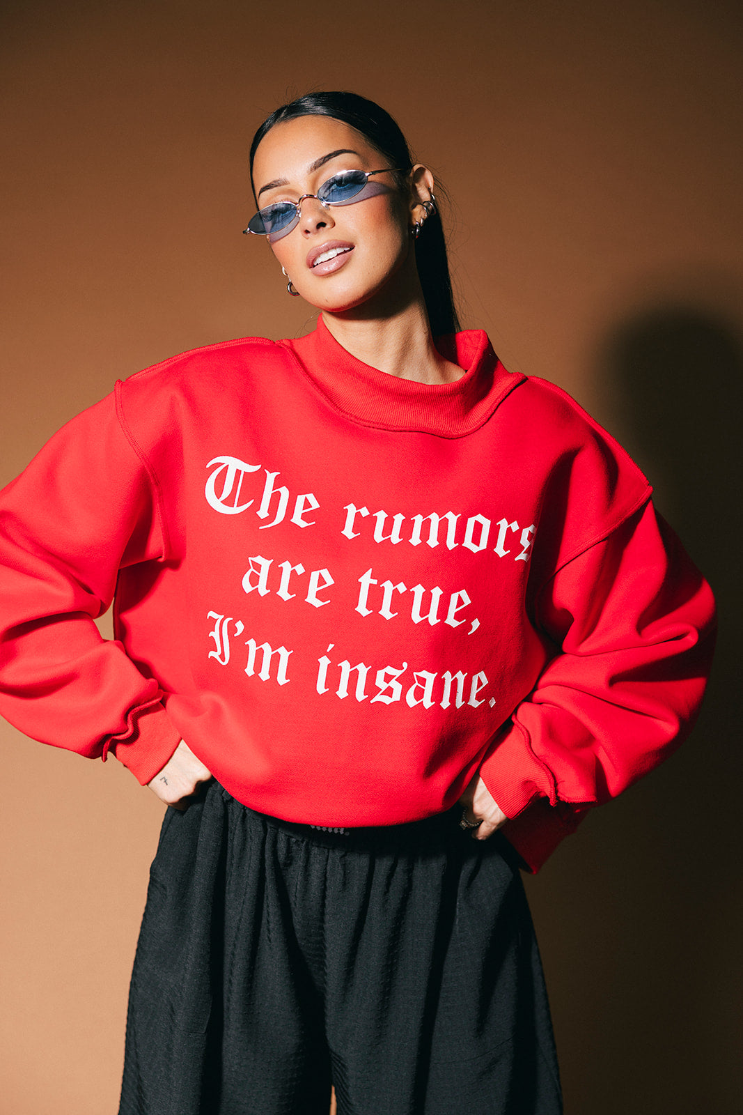 Person wearing a red sweatshirt with text, standing against a brown background