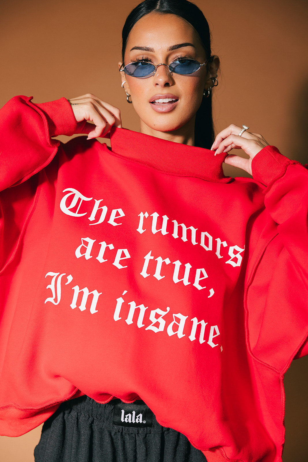 Person wearing a red sweatshirt with text, holding it up in front of a brown background