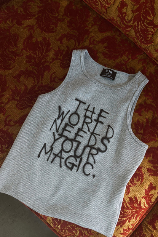 Gray tank top with 'The World Needs Your Magic' text on a patterned couch