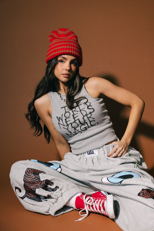 Woman wearing a gray tank top with text and patterned pants sitting on a brown background