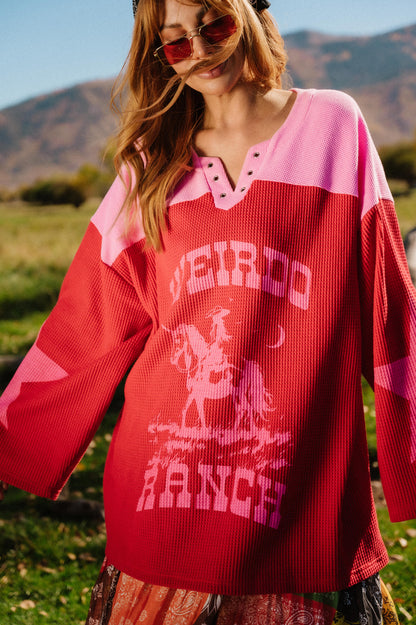 Person wearing a red and pink waffle knit hockey jersey inspired top with 'Weirdo Ranch' text and cowgirl riding a unicorn graphics in an outdoor setting