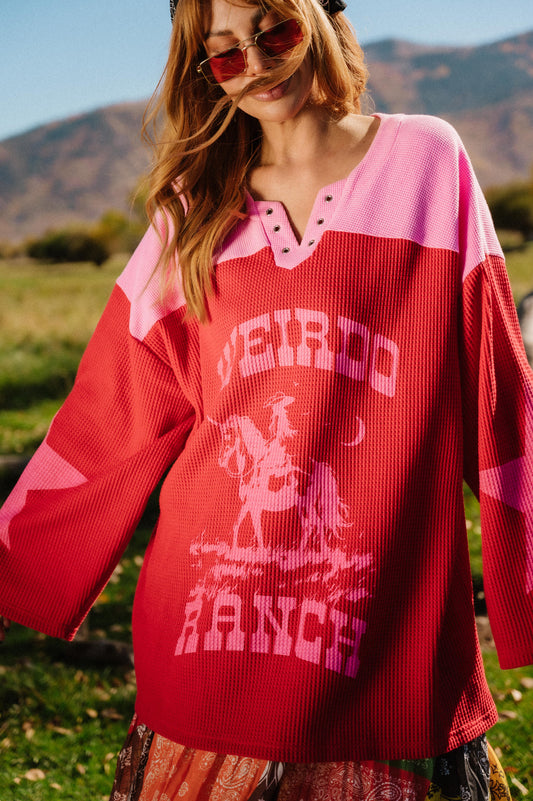 Person wearing a red and pink waffle knit hockey jersey inspired top with 'Weirdo Ranch' text and cowgirl riding a unicorn graphics in an outdoor setting