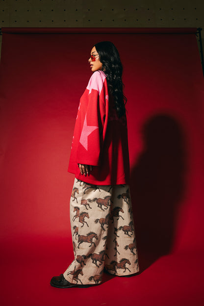 Person wearing a red and pink waffle knit hockey jersey inspired top with star graphics on the sleeves against a red background