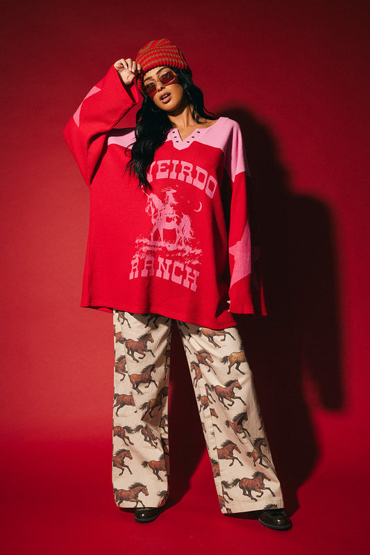 Person wearing a red and pink waffle knit hockey jersey inspired top with 'Weirdo Ranch' text and cowgirl riding a unicorn graphic on a red background