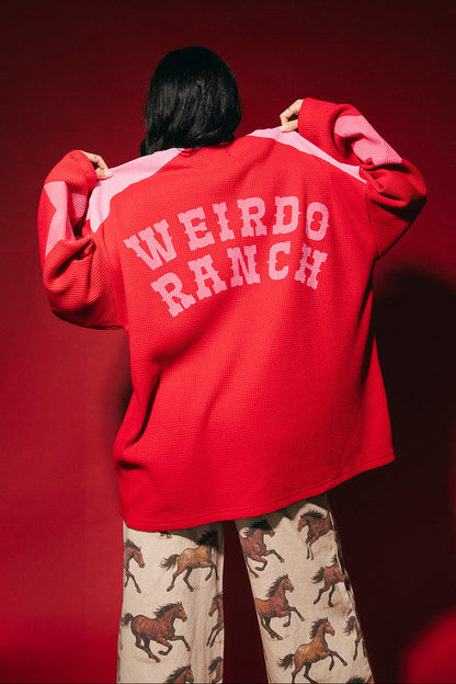 Person wearing a red and pink waffle knit hockey jersey inspired top with 'WEIRDO RANCH' text on a red background