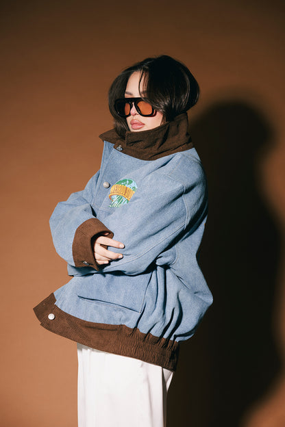 Person wearing a blue denim jacket with brown corduroy details against a brown background