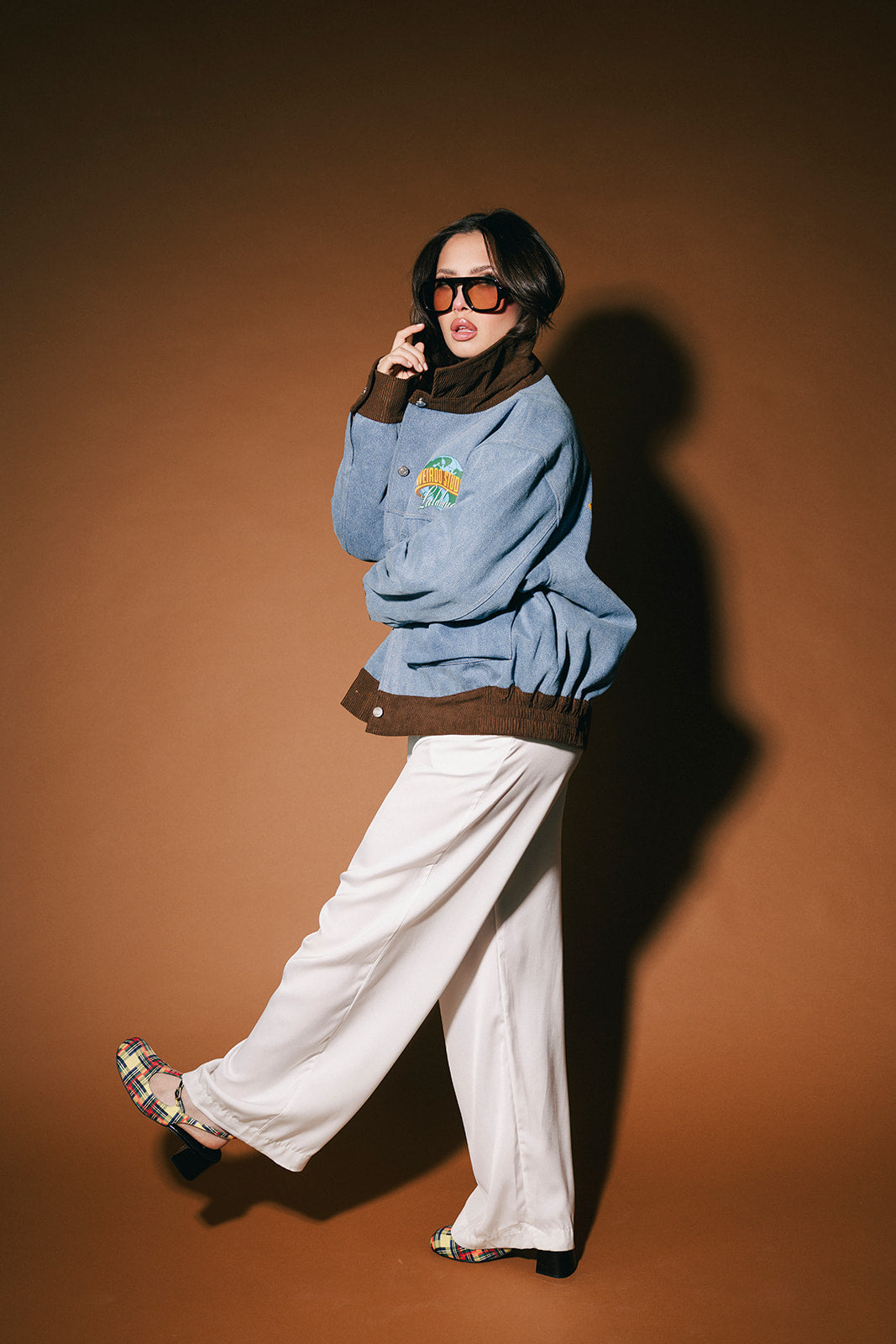Person wearing a blue denim jacket and white pants against a brown background