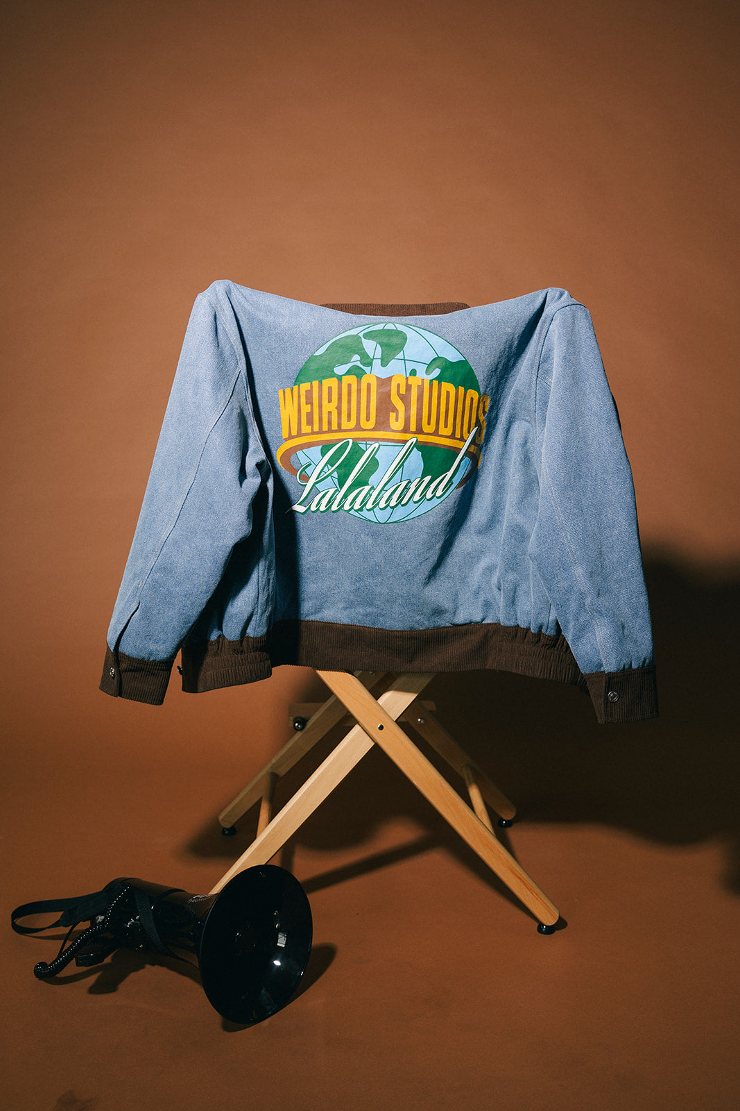 Blue denim jacket with 'Weirdo Studios Lalaland' logo on a brown background