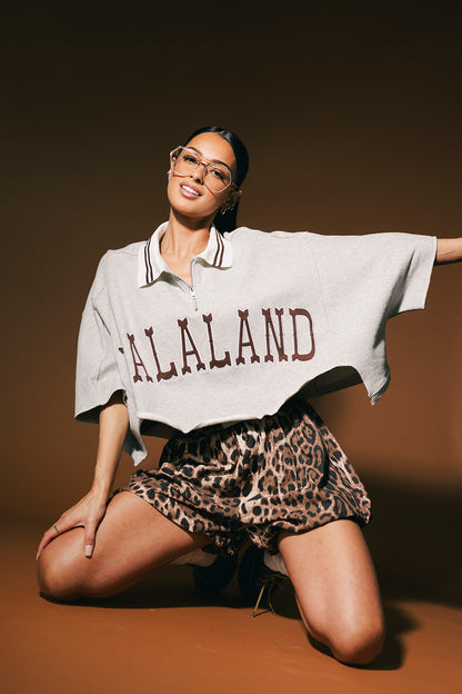 Woman wearing a 'LALALAND' polo and leopard print shorts on a brown background