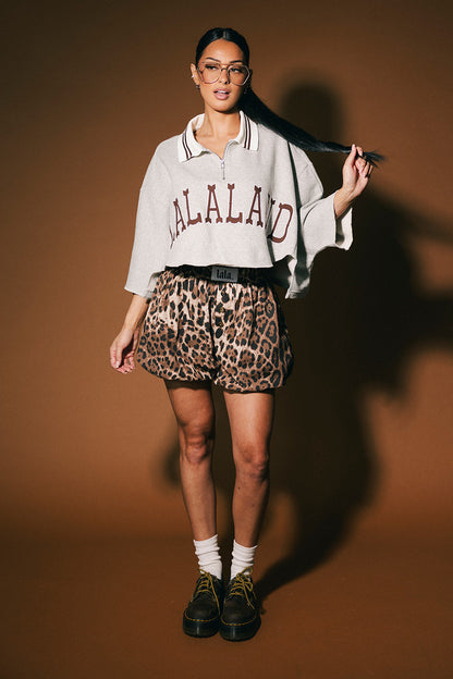 Person wearing a grey polo with text and leopard print shorts against a brown background