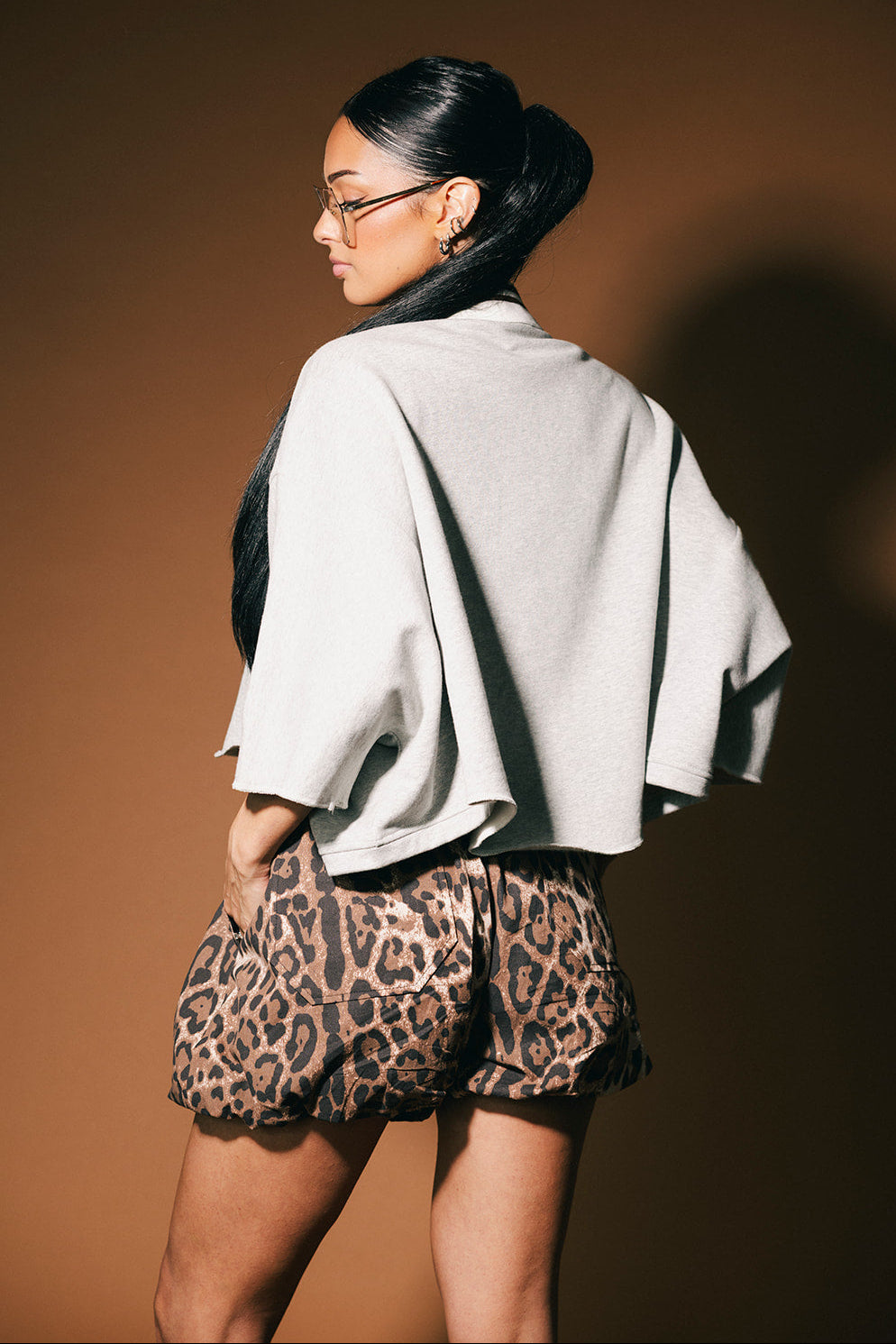 Woman wearing a gray polo and leopard print shorts against a brown background