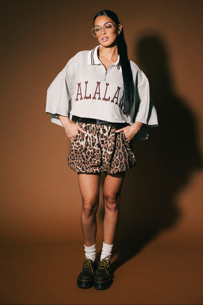 Person wearing a 'LALALAND' polo with leopard print shorts on a brown background