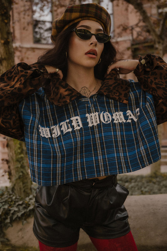 Person wearing a blue plaid shirt with 'WILD WOMAN' text, leopard print sleeves and collar, and sunglasses outdoors.