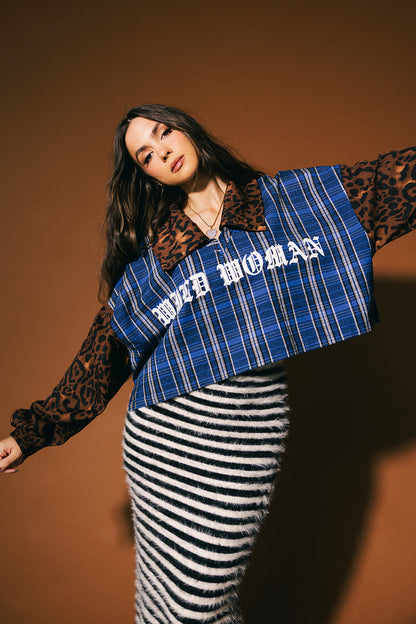Woman wearing a blue plaid shirt with 'Wild Woman' text with leopard sleeves and collar against a brown background.