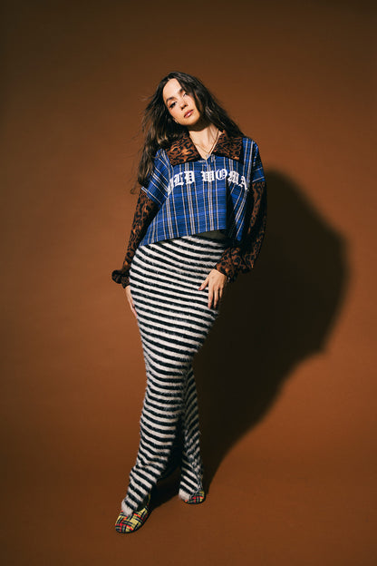 Woman wearing a blue plaid shirt with 'Wild Woman' text on the front and leopard print sleeves and collar against a brown background.