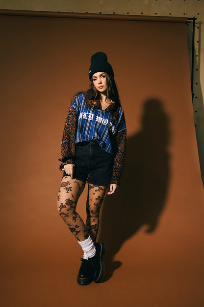Woman wearing a blue plaid top with 'Wild Woman' on the front and leopard print sleeves and collar against a brown background.