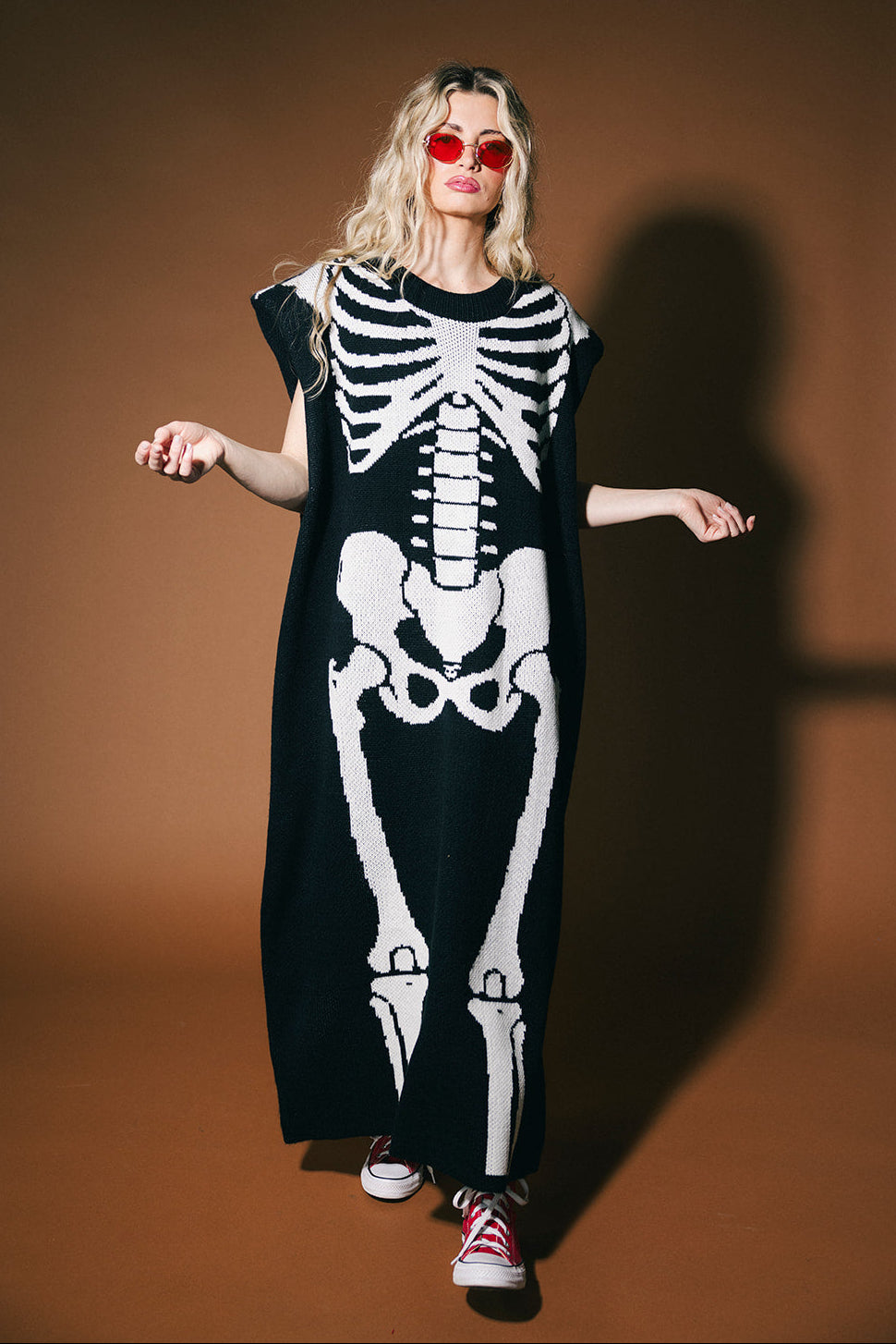 Person wearing a long black dress with a white skeleton design on a brown background