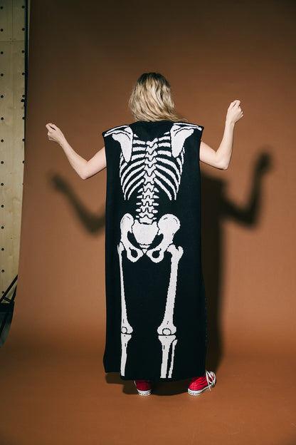 Person wearing a black sleeveless dress with a white skeleton design on a brown background