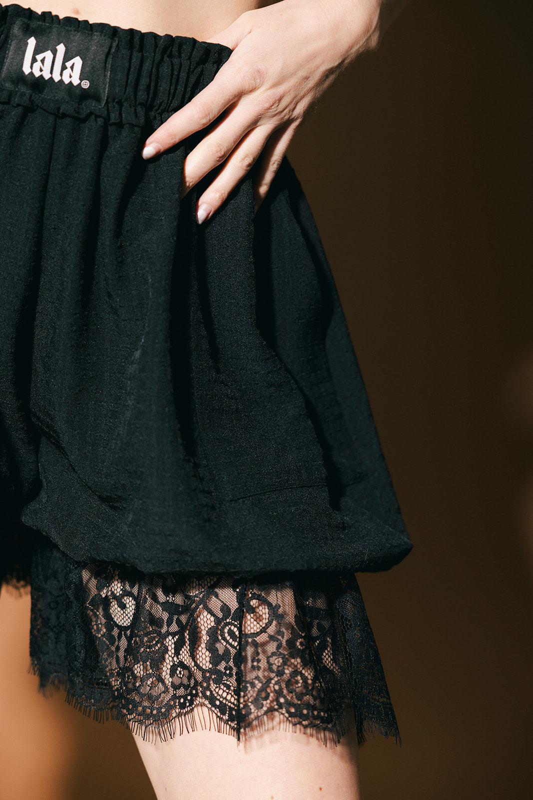 Black lace-trimmed shorts with 'lala' branding on a brown background