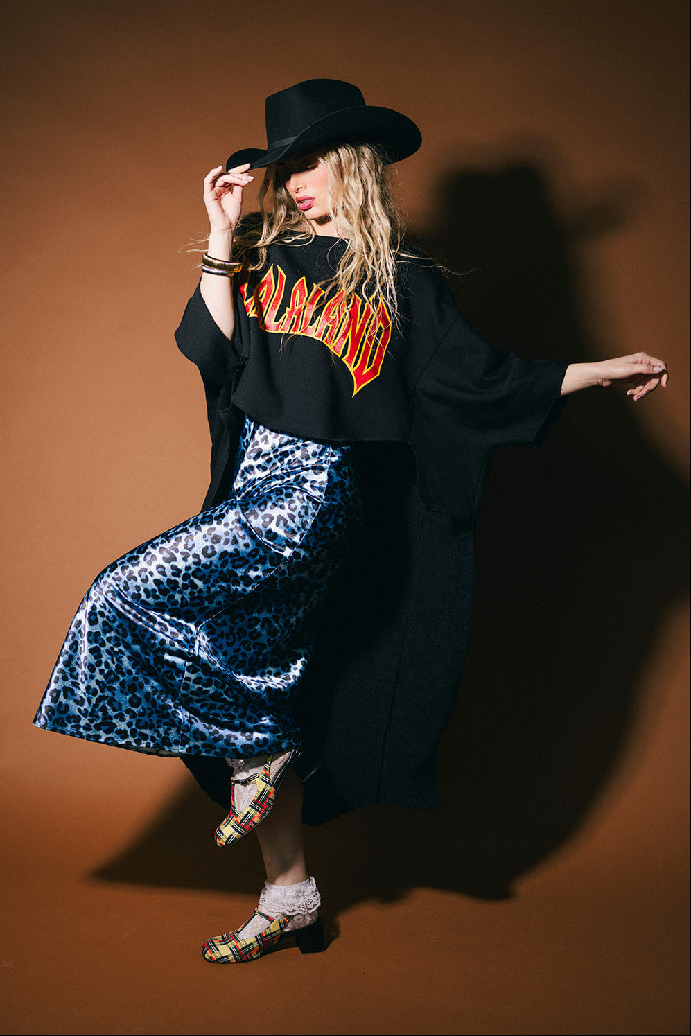 Woman wearing a black cowboy hat and a black jacket with a patterned dress against a brown background